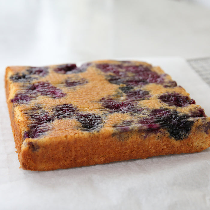 Close-up side view of a square Einkorn blueberry upside-down cake showing baked blueberries and a golden-brown crust on parchment