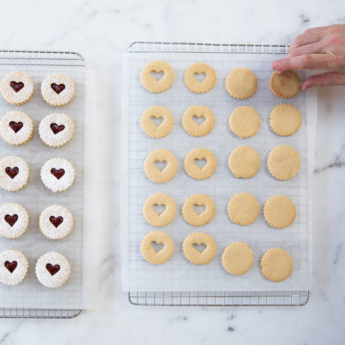 Overhead view of Einkorn Linzer cookies with heart cutouts, powdered-sugar tops and jam centers on parchment-lined racks