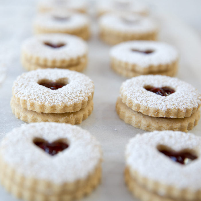 Close-up of Linzer cookies made with Einkorn, heart-shaped jam centers dusted with powdered sugar, arranged in two rows on parchment paper