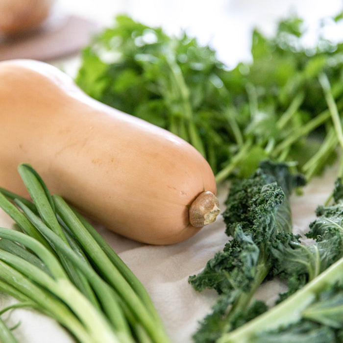 Close-up of a whole organic butternut squash with green onions and curly kale on a white cloth, ingredients for vegetarian chili