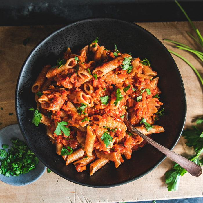 Bowl of organic whole wheat penne in eggplant bolognese sauce, garnished with parsley on a wooden table