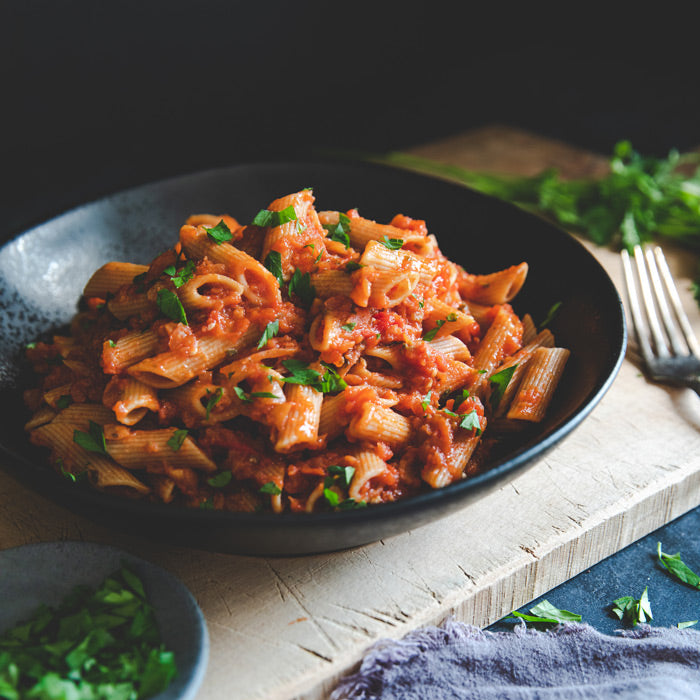Bowl of organic whole wheat penne rigate tossed in eggplant bolognese sauce on a rustic wooden table