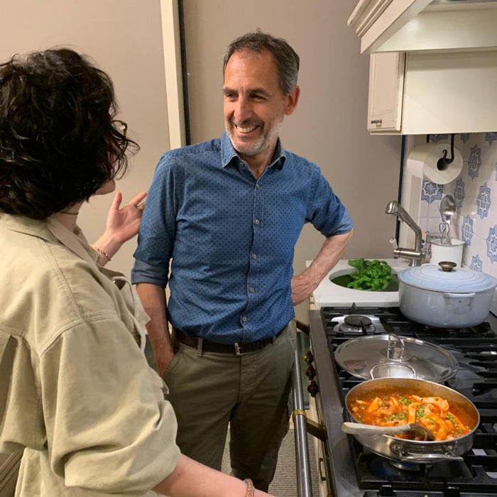 Calamari in tomato sauce simmering in a skillet on the stovetop while two people chat in a home kitchen
