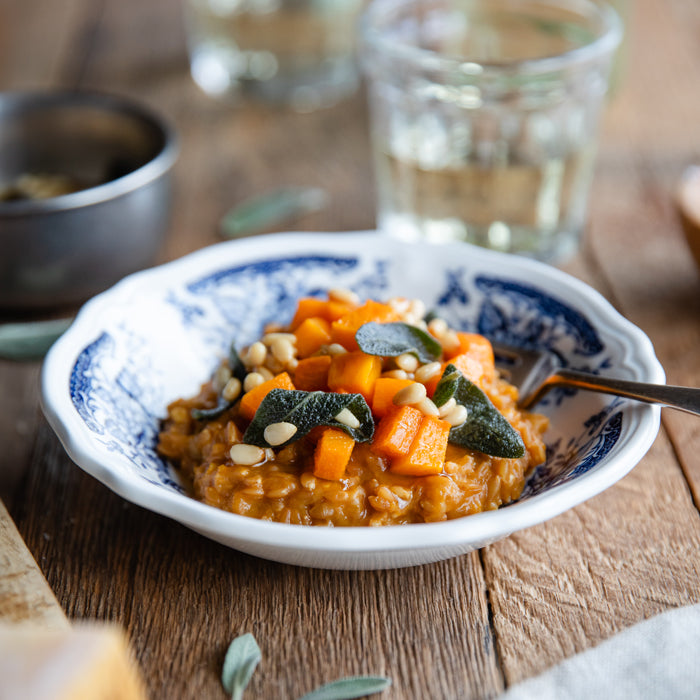 Bowl of einkorn wheat berry risotto with roasted butternut squash, fried sage leaves, and toasted pine nuts on a wooden table