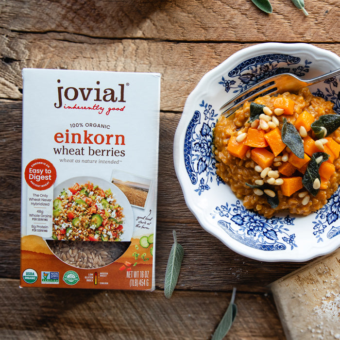 Top-down of Jovial einkorn wheat berries box beside a bowl of butternut squash and sage wheat-berry risotto on a wooden surface