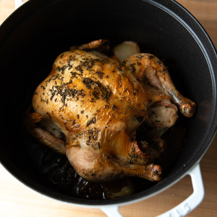 Whole roasted chicken resting in a Dutch oven seasoned with herbs and caramelized onions