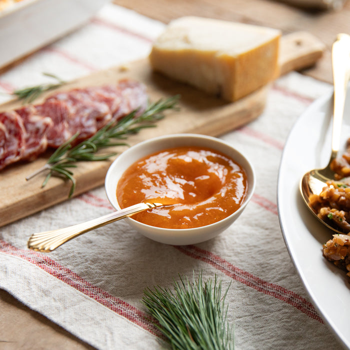 Bowl of apricot sauce sitting on a striped cloth beside a platter of wheat‑berry stuffing, salami, and cheese