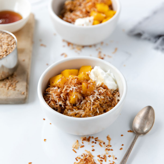 Ancient grain wheat berry bowl with diced mango, toasted coconut flakes and yogurt on a white tabletop