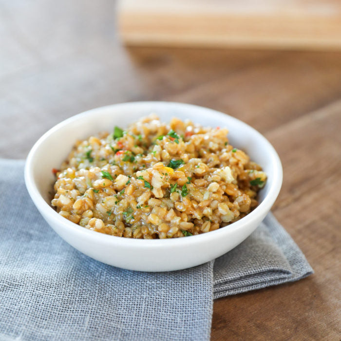 Front view of bowl of cooked wheat berries showcasing chewy whole-grain texture and chopped herbs on a gray napkin