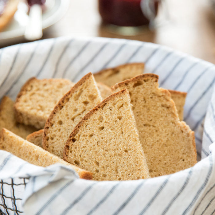 Close-up of sliced Einkorn whole wheat sandwich bread showing dense crumb and golden crust in a striped cloth lined basket