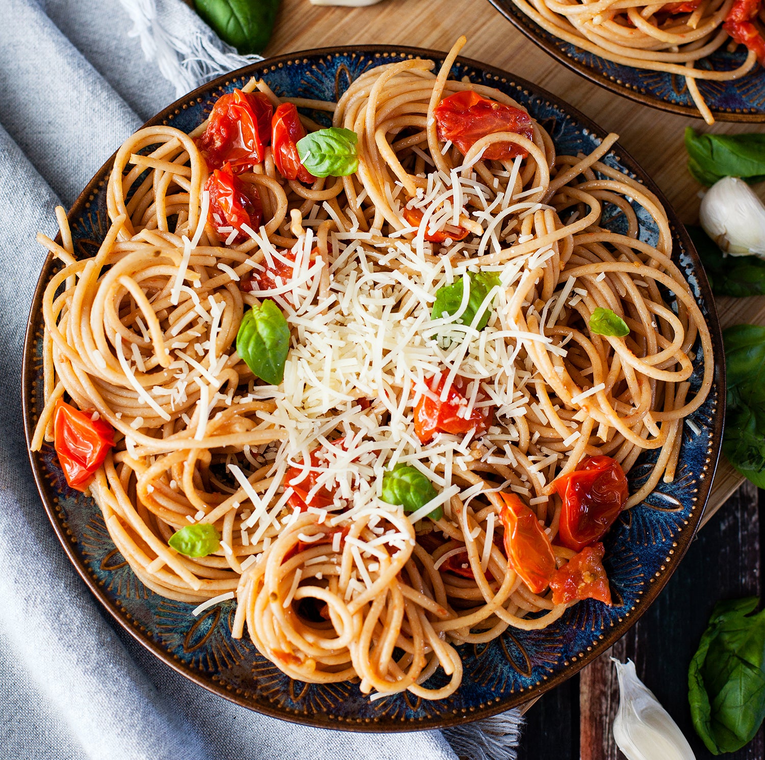 Organic whole wheat spaghetti tossed with sun-dried tomato pesto, topped with grated cheese and fresh basil on a dark plate