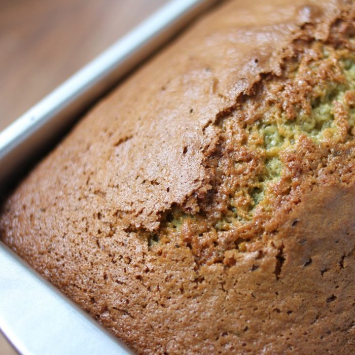 Close-up of Einkorn zucchini bread loaf showing golden-brown crust and green zucchini-flecked crumb in a metal loaf pan