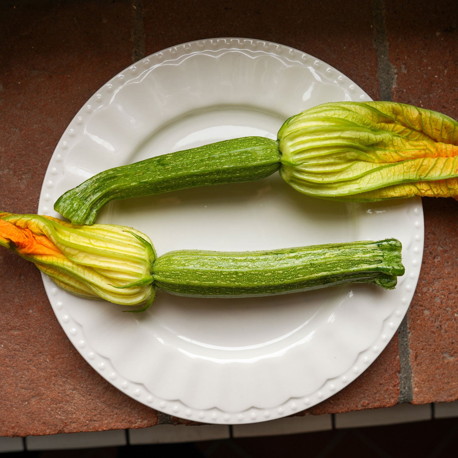 2 fresh spring zucchine with the flowers attached, on a plate
