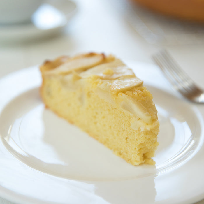 Three-quarter side view of a slice of Einkorn apple breakfast cake showcasing its tender golden crumb and thin baked apple slices on a white plate