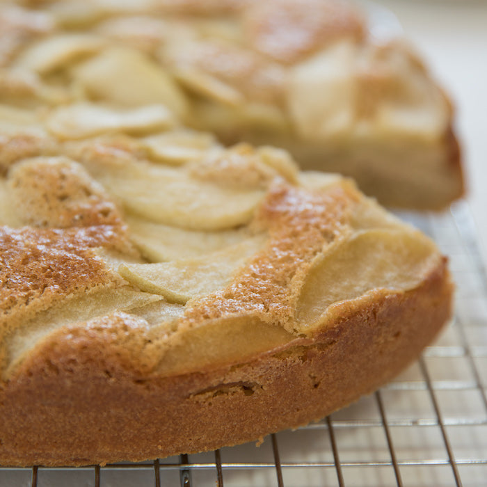 Close-up side view of a gluten-free Einkorn apple breakfast cake showing golden crust and layered apple slices on a cooling rack