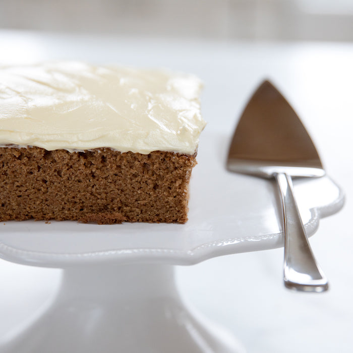 Slice of applesauce cake on a white cake stand with a server, showcasing a recipe made with einkorn flour