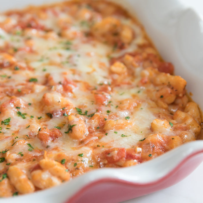 Close-up of baked cannellini beans in a red-rimmed ceramic baking dish showcasing melted browned cheese and chopped parsley