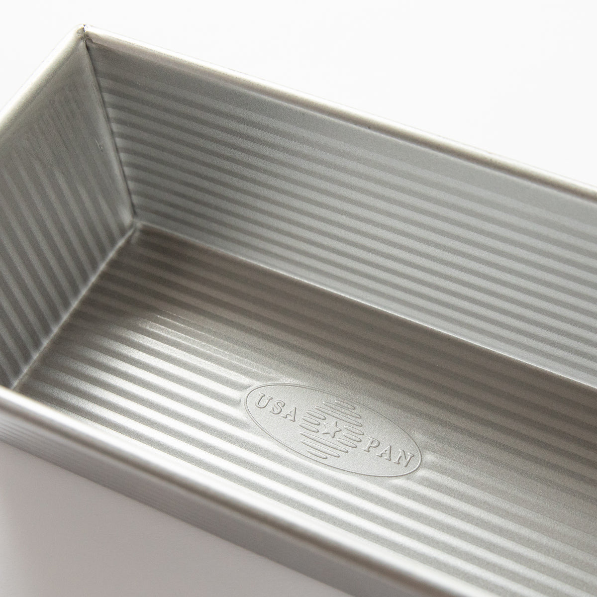 Angled close-up of metal loaf pan showing ridged interior and embossed marking on bottom with white background