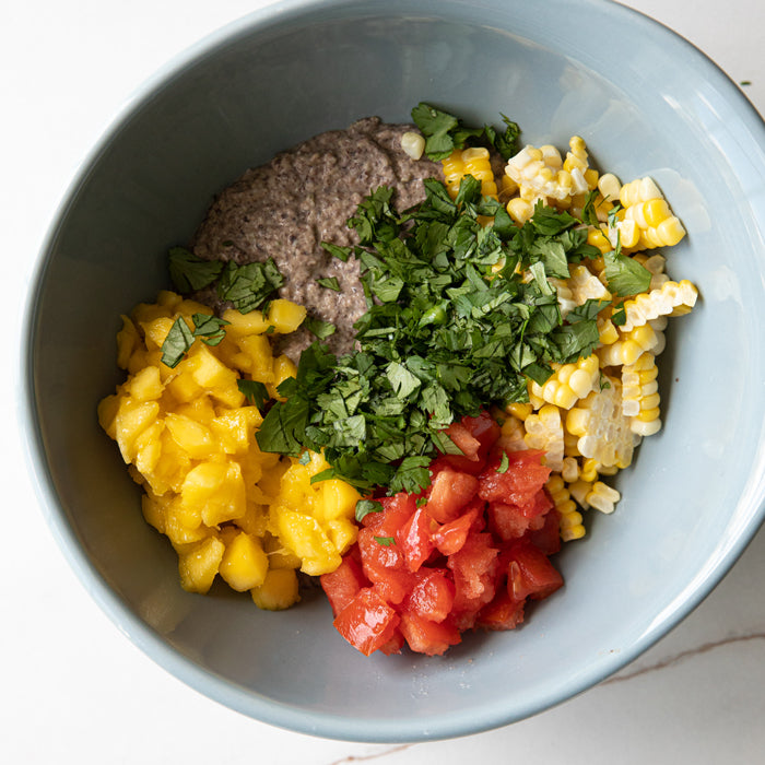 Bowl of organic black bean dip topped with diced mango, tomato, corn, and chopped cilantro