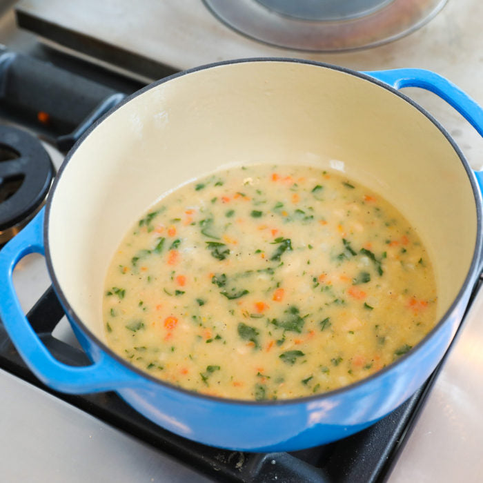 Cannellini and potato vegetable soup with spinach and diced carrots simmering in a blue enameled Dutch oven on a gas stove