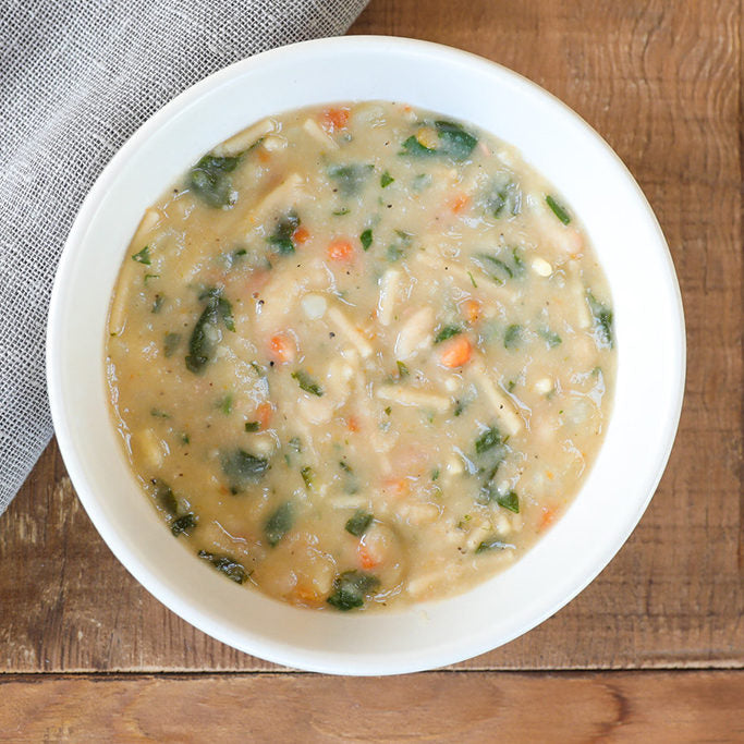 Top-down view of cannellini and potato soup in a white bowl with creamy broth, spinach, carrots, and cannellini beans