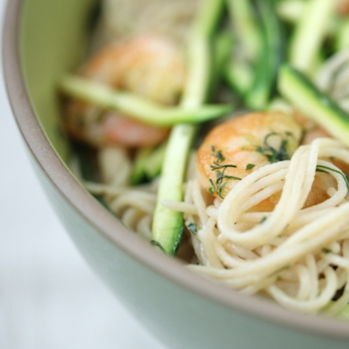 Bowl of cooked organic gluten free brown rice capellini with shrimp, asparagus, and dill served in a green bowl