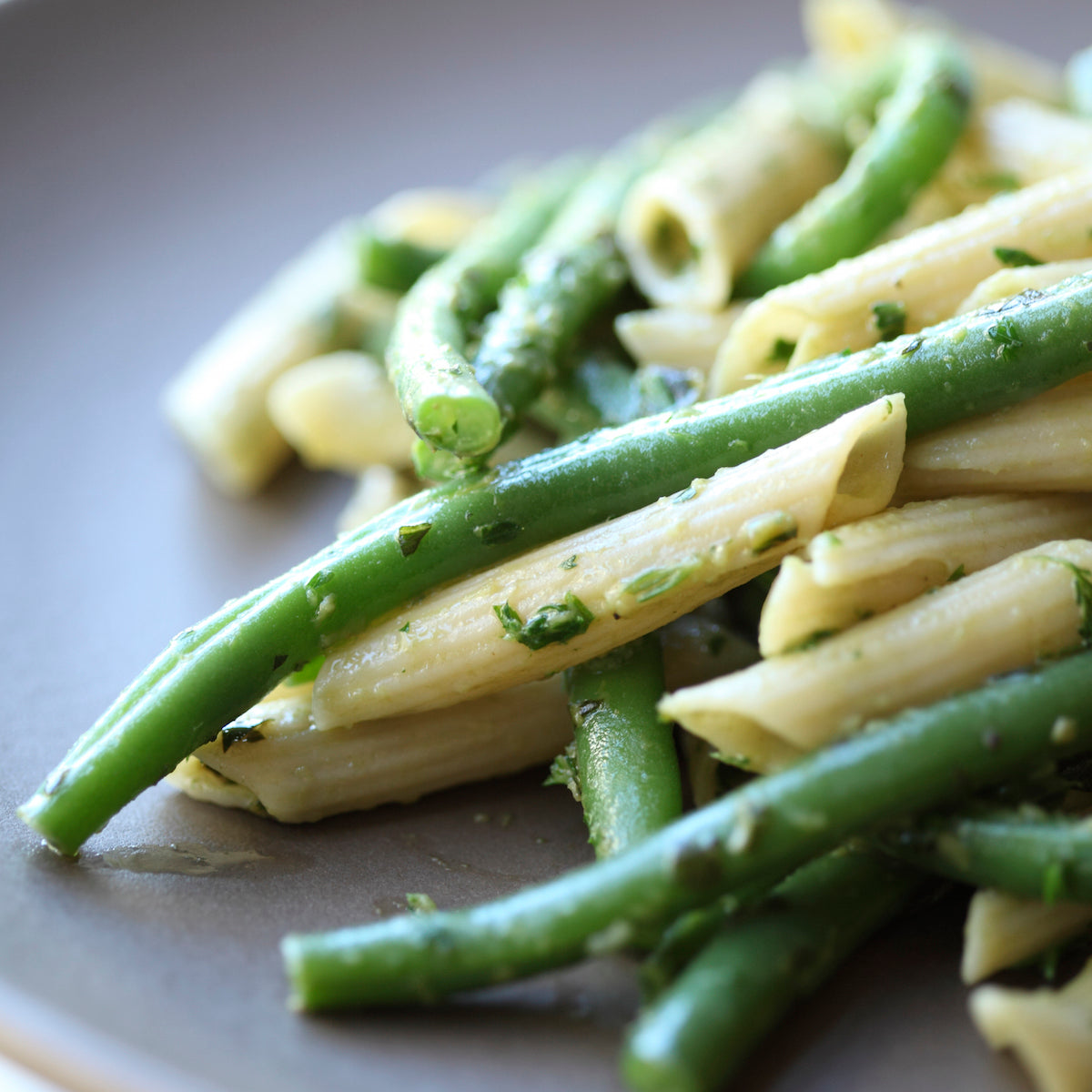 Cooked organic brown rice penne rigate tossed with green beans on a gray plate