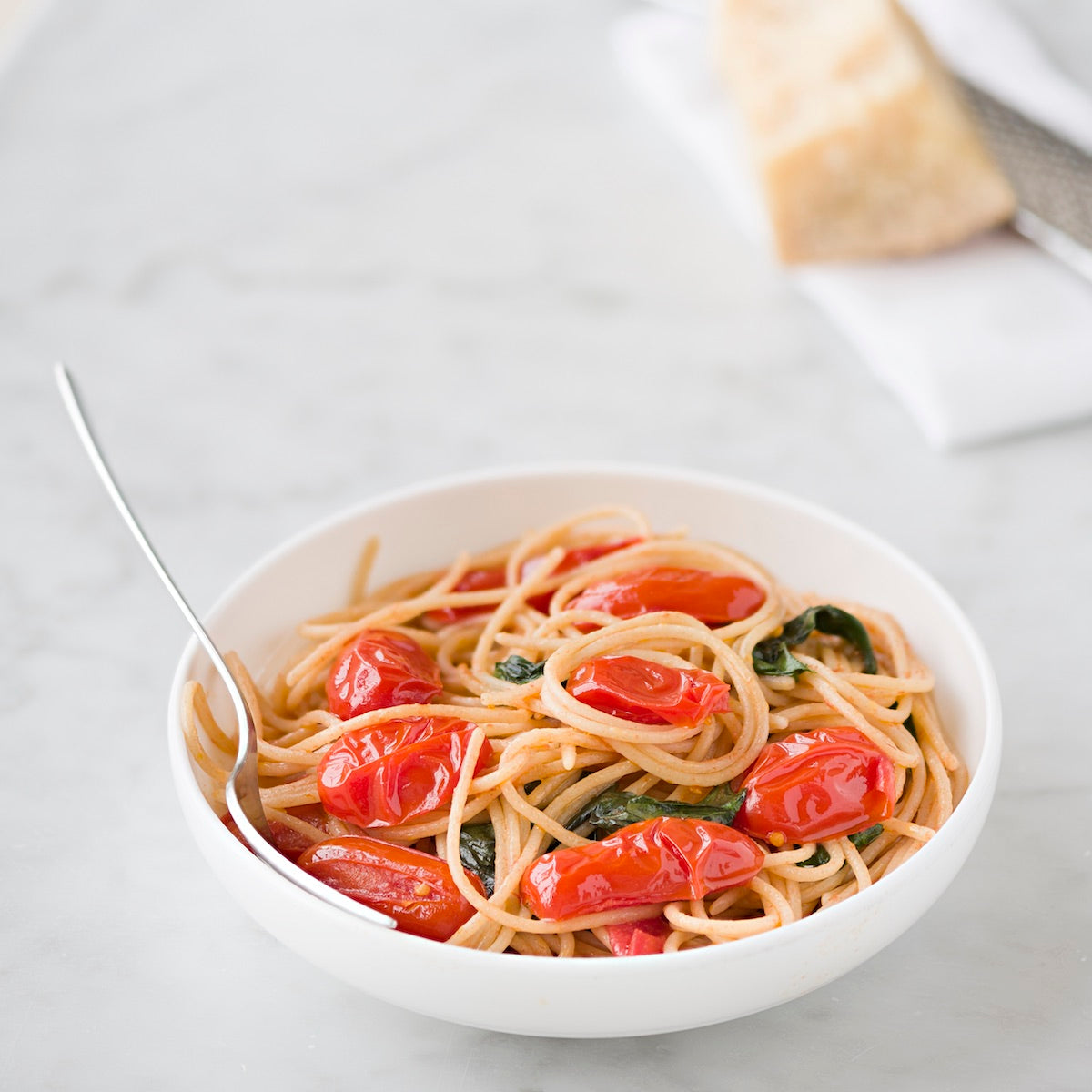 Bowl of organic gluten-free brown rice spaghetti with cherry tomatoes and basil on a light marble tabletop