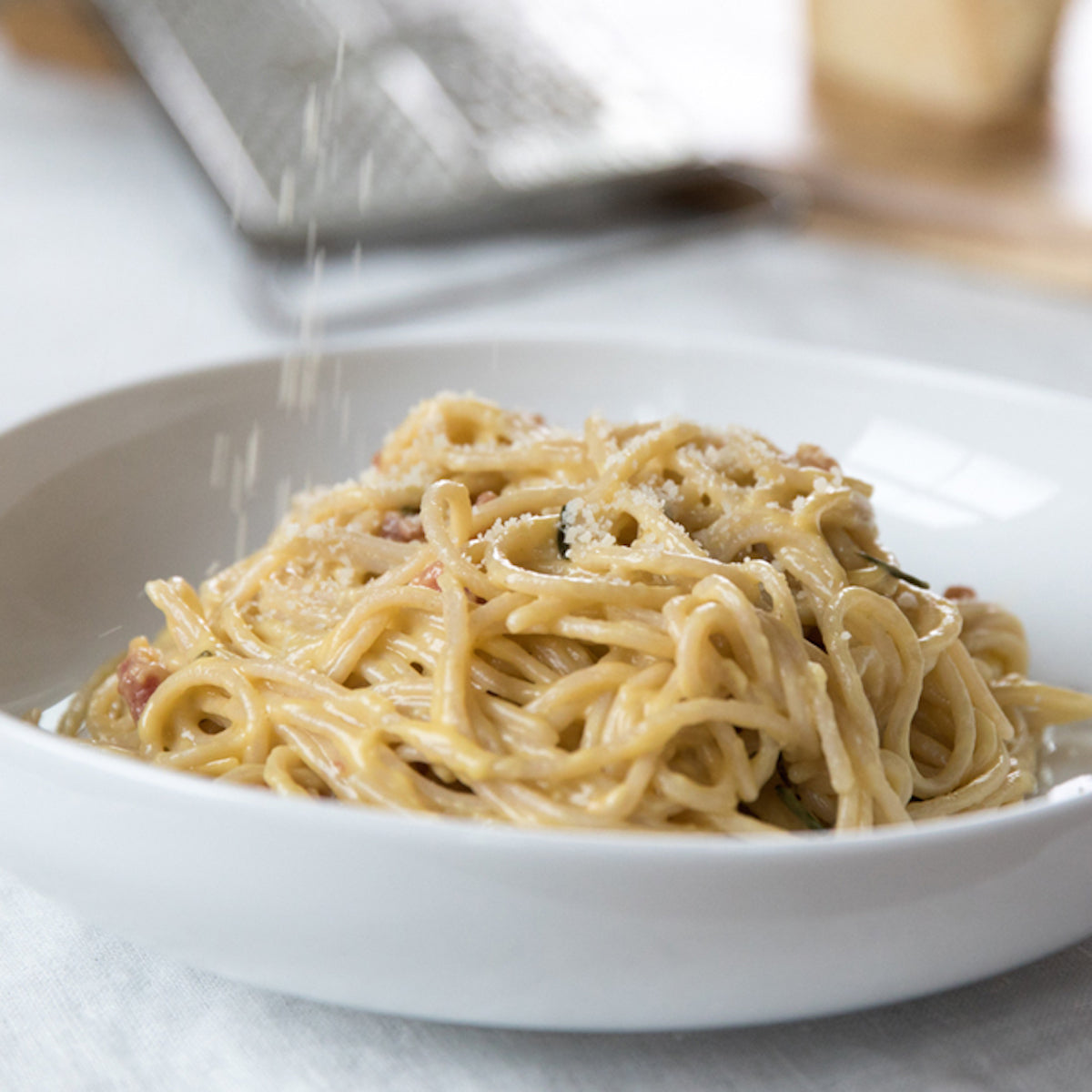Cooked organic brown rice spaghetti served as creamy carbonara garnished with rosemary on a white plate
