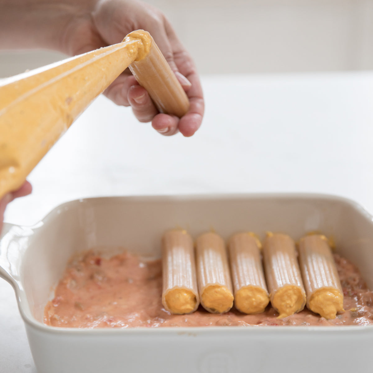 Hand filling organic gluten-free brown rice manicotti with butternut squash and tomato filling in a casserole dish