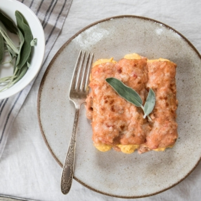 Top view of butternut squash-filled manicotti in tomato-cream sauce garnished with sage on a gray ceramic plate with fork