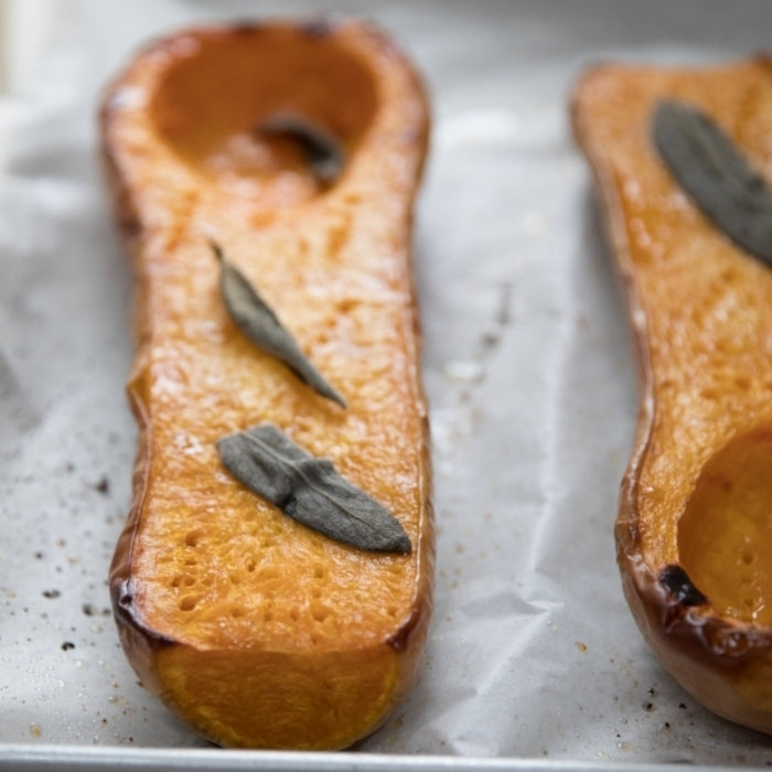 Roasted butternut squash halves garnished with sage on a parchment-lined baking sheet