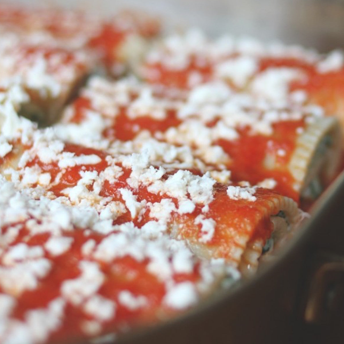 Gluten free brown rice manicotti in a baking dish topped with tomato sauce and grated cheese, ready to bake