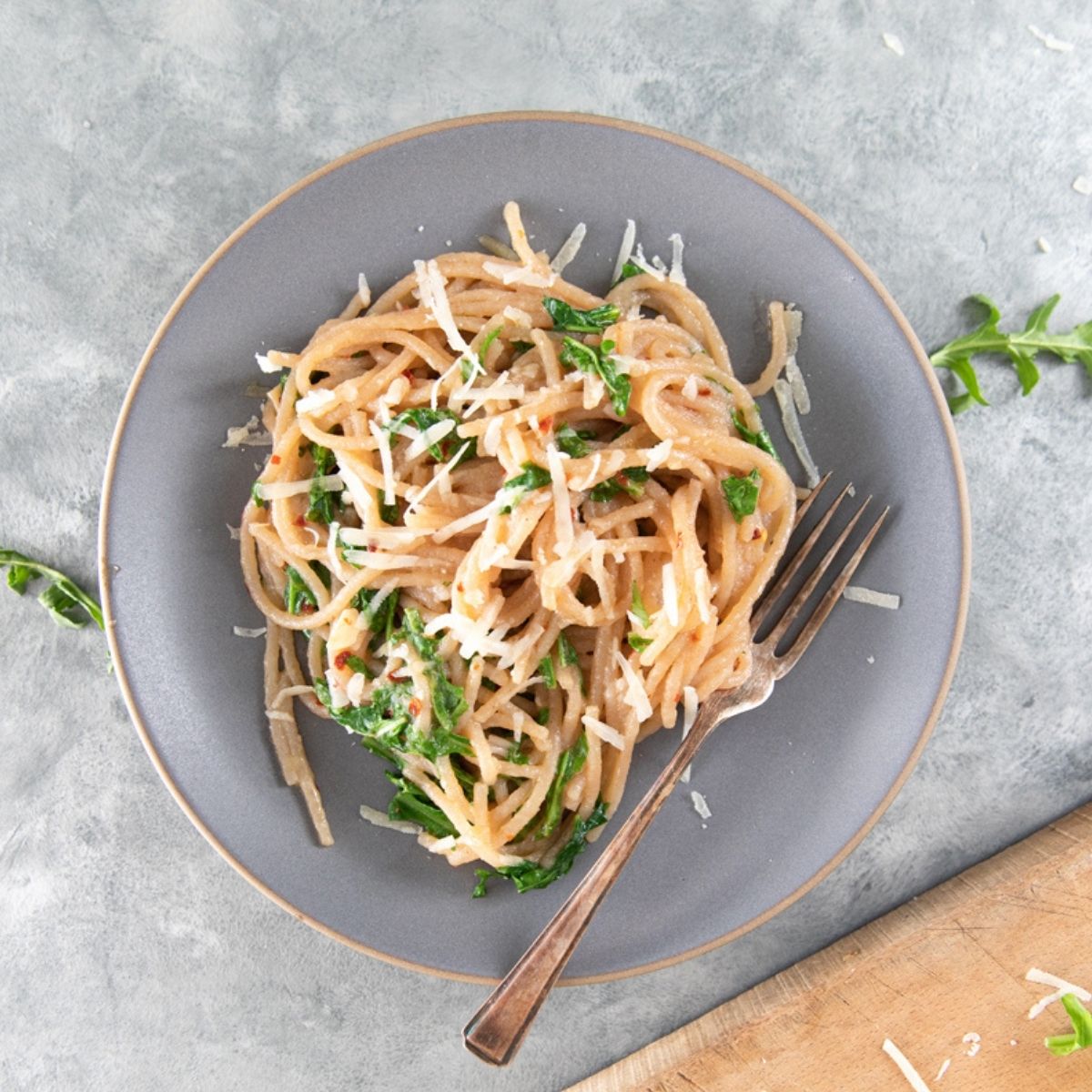 Plated cooked organic cassava spaghetti with grated cheese and parsley on a gray plate