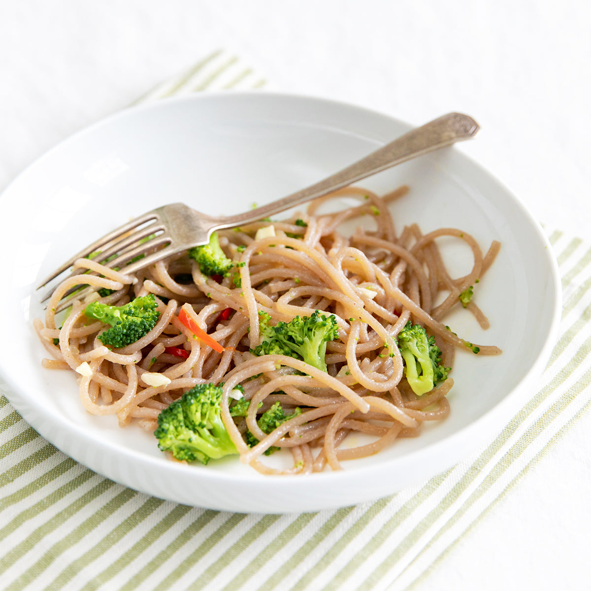 Bowl of cooked organic, gluten-free cassava spaghetti with broccoli and a fork on a striped napkin