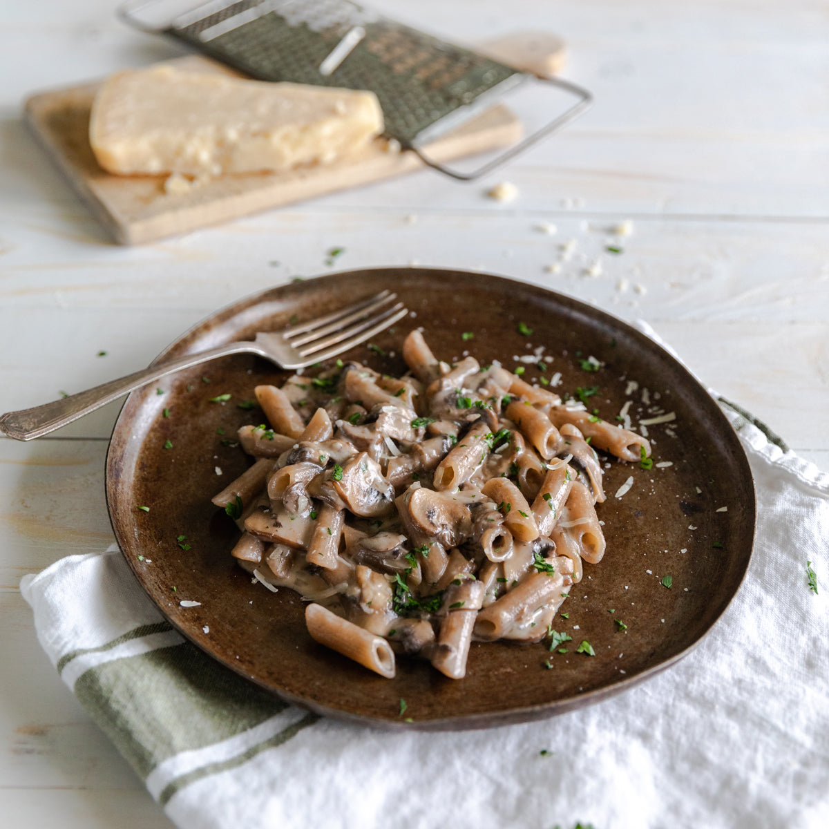 Organic cassava penne in creamy mushroom sauce served on a brown plate with grated cheese and a fork on a linen napkin