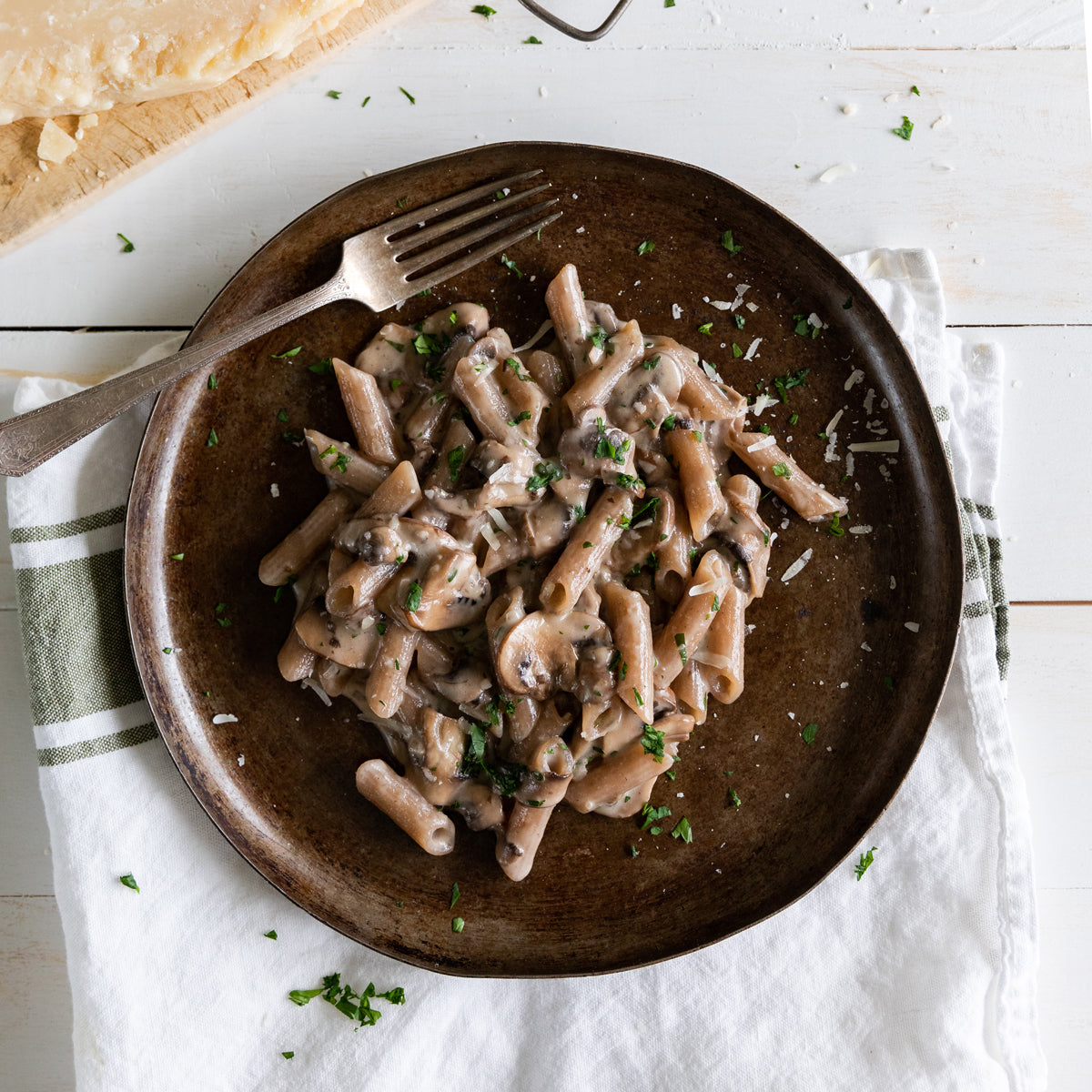 Organic cassava penne in creamy mushroom sauce on a brown plate with a fork and white cloth napkin