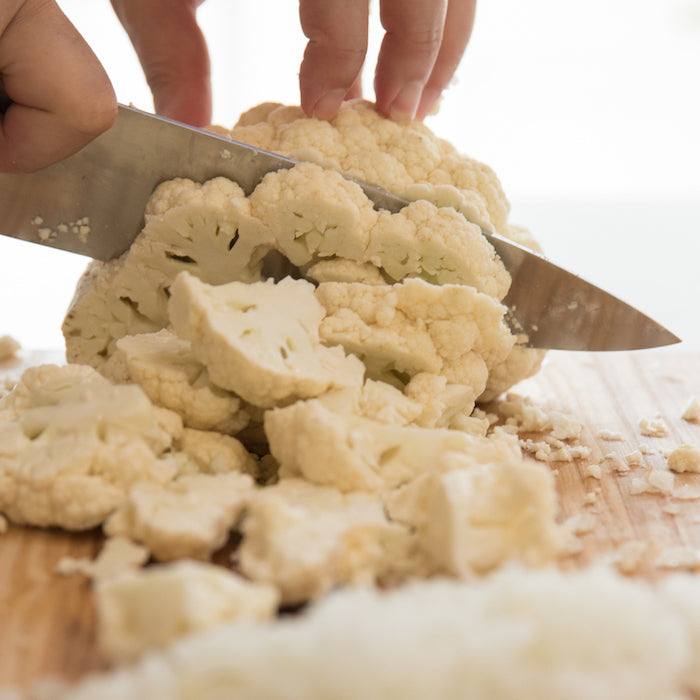 Hands slicing cauliflower into florets on a wooden cutting board for a gluten-free spaghetti recipe