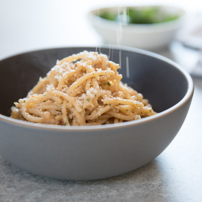 Gluten-free spaghetti tossed with pan-roasted cauliflower and grated cheese in a gray bowl on countertop