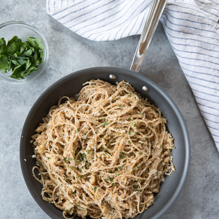 Pan-roasted cauliflower tossed with gluten-free spaghetti in a skillet, garnished with chopped parsley and a striped kitchen towel nearby