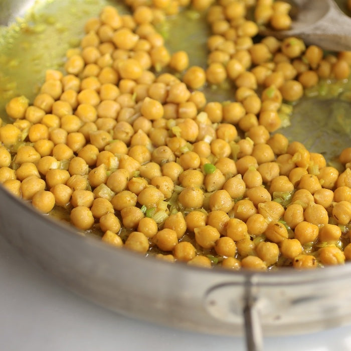 Close-up of sauteed chickpeas in a skillet showcasing golden color, olive oil sheen, and bits of sautéed onion on a light surface