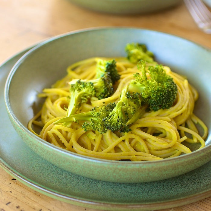 Bowl of Jovial spaghetti tossed in creamy chickpea sauce with roasted broccoli in a green ceramic bowl on a wooden table