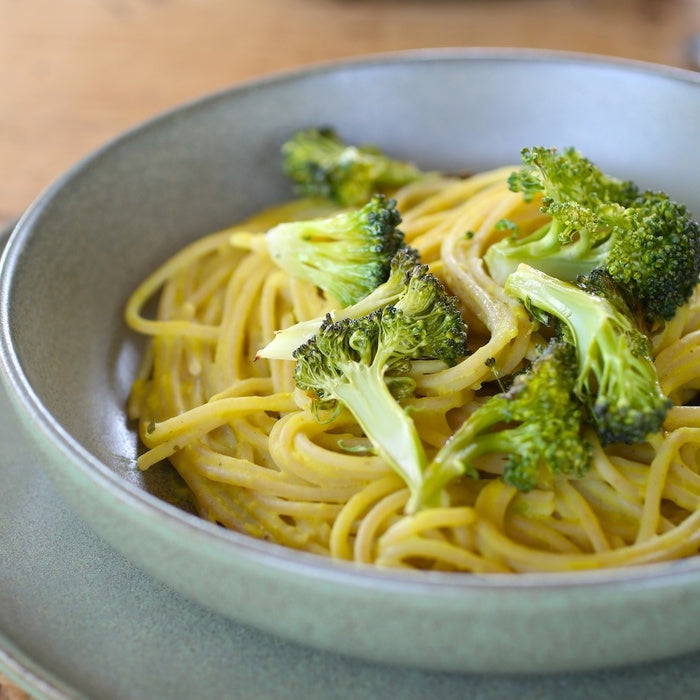 Jovial spaghetti in creamy chickpea sauce with roasted broccoli in a green ceramic bowl