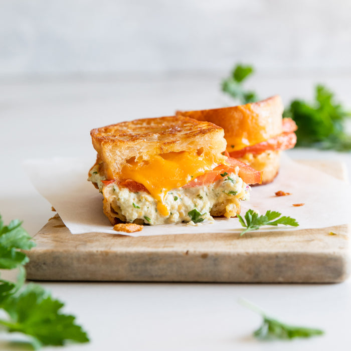 Angled view of chickpea tuna melt sandwich with melted vegan cheese, tomato and parsley on toasted bread, marble background