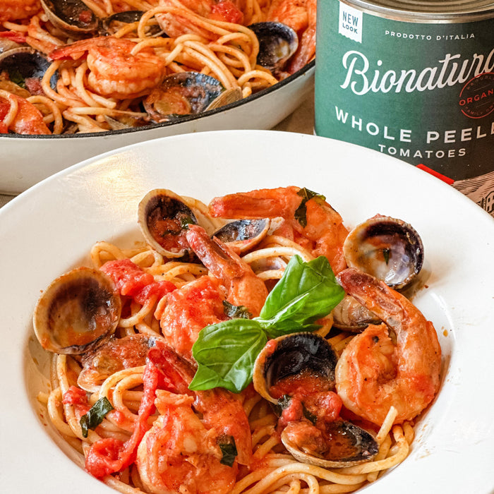 Bowl of spaghetti with clams and shrimp in tomato sauce, garnished with fresh basil