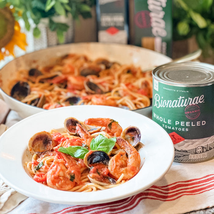 Bowl of spaghetti with clams and shrimp in tomato sauce, basil garnish, can of Bionaturae whole peeled tomatoes beside it