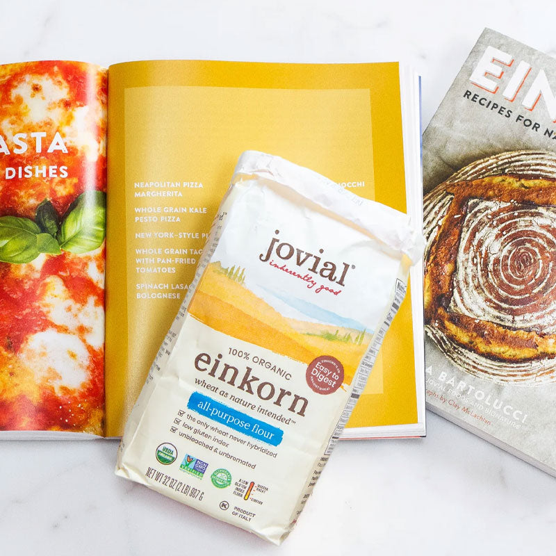 Angled front view of Jovial Einkorn all-purpose flour bag showing 100 percent organic label with open cookbook in the background
