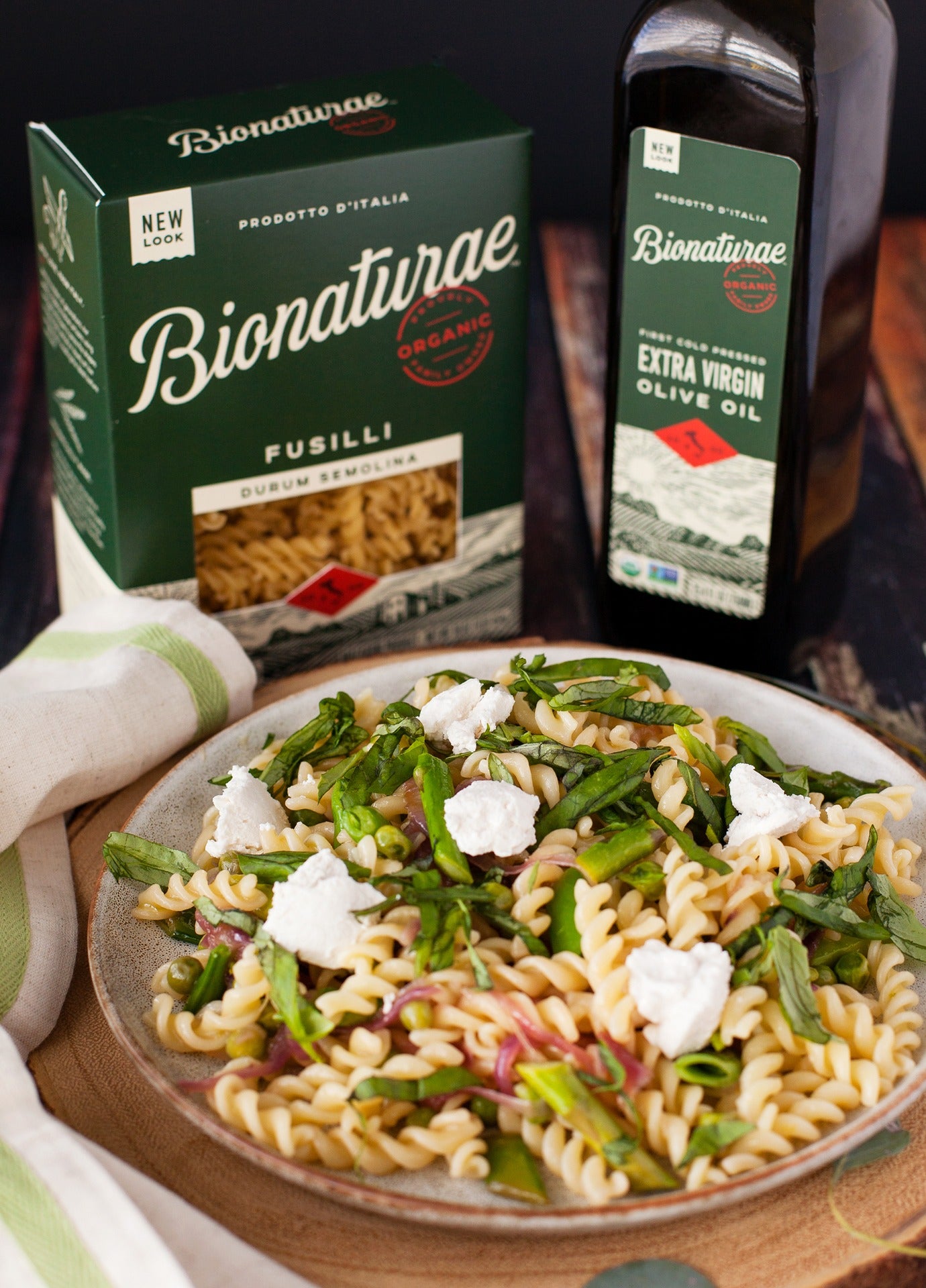 Plate of fusilli pasta with greens and ricotta, served in front of a Bionaturae fusilli box and organic extra virgin olive oil bottle
