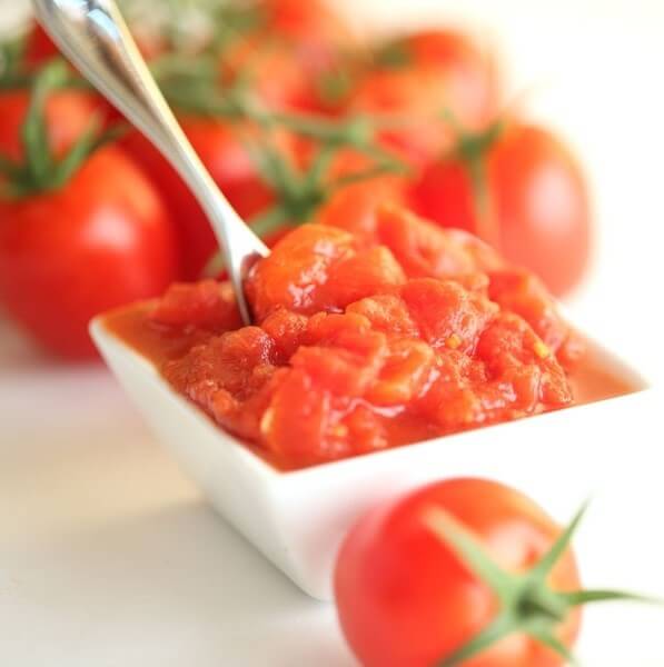 Close-up of Organic Italian diced tomatoes in a white square bowl showcasing chunky, saucy texture with whole tomatoes blurred behind