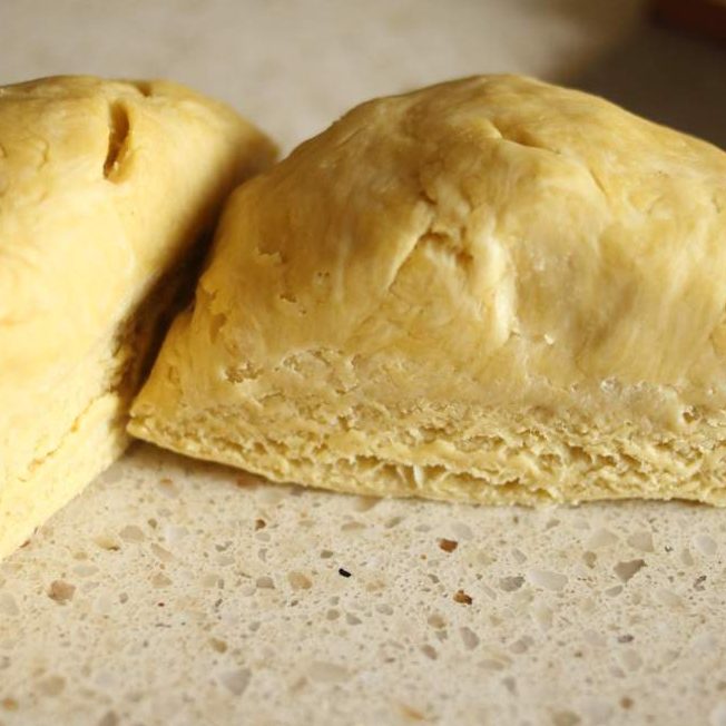 Close-up of Einkorn pie dough divided into two pieces showing layered, flaky texture on a speckled countertop